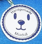 Runder handmade Medaillon mit einem niedlichen Hundegesicht, umgeben von einem blauen Rahmen, mit der Aufschrift 'Handgemacht' und 'Miadoll' für handgefertigte Tieraccessoires.