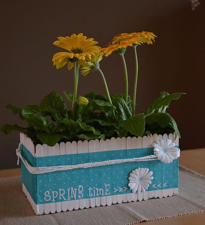 Blumenkiste mit gelben Frühlingsblumen, dekorativ und bunt, passend für Frühling und Garten, mit weißen Blüten und blauer Dekoration, handgemacht, für kreative Dekorationen.
