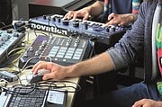 Zwei Personen arbeiten an Musikproduktions-Equipment mit MIDI-Controllern, Mixer und Laptop, kreative Musikgestaltung im Studio.