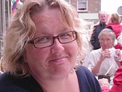 Porträt einer Frau mit Brille und lockigem Haar bei HANDMADE Kultur Veranstaltung, umgeben von anderen Menschen, die handgemachte Produkte genießen.