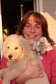 Frau hält einen süßen, hellen Hundewelpen, lächelnd, bei einem Outdoor-Event, mit Fokus auf Tierliebe und handgemachte Kultur.