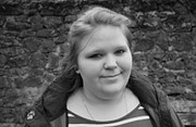 Porträt einer jungen Frau mit einem freundlichen Lächeln, umgeben von handgefertigten Kunstwerken und kreativen Materialien, die die Vielfalt und Qualität der HANDMADE Kultur zeigen.
