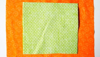 Helles grünes Stoffquadrat mit weißen Punkten, geeignet für Näharbeiten wie Plissee oder Innentaschen, auf orangefarbenem Hintergrund mit Blumenmuster.