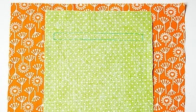 Nähen einer Innentasche aus grüner Baumwolle mit weißem Punktmuster, auf orangefarbenem Stoff mit Blumenmuster, für Sew Along Tag 3: Plissee und Innentasche nähen.