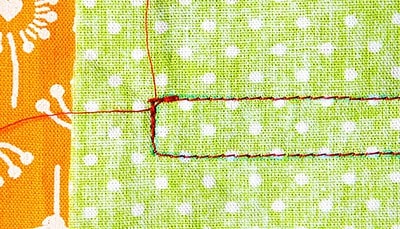 Detailaufnahme einer grünen Stoffbahn mit weißem Punktmuster, rote Nähte und eine aufgenähte Tasche, passend zum Sew Along Tag 3: Plissee und Innentasche nähen.