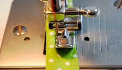 Nähmaschine näht grünen Stoff mit weißen Punkten, Fokus auf Nähprozess und Stoffdetails.