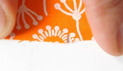 Nahaufnahme eines Stoffstücks mit orangefarbenem Blumenmuster, geeignet für Näharbeiten wie Plissee oder Innentaschen, im Rahmen eines Sew Along.