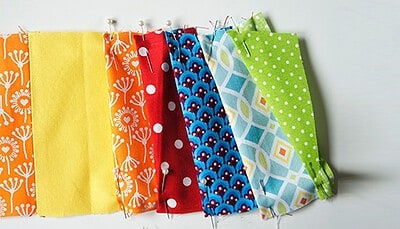 Verschiedene bunte Stoffe mit Mustern, bereit für Näharbeiten, in einer Reihe aufgehängt, ideal für kreative Handarbeiten und DIY-Projekte.