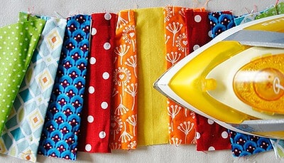Verschiedene bunte Stoffe mit Mustern, bereit für das Nähen von Plissee und Innentaschen, inklusive Bügeleisen für Textilarbeiten.