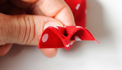 Nähen einer Stoffblume mit rotem Stoff mit weißen Punkten, Teil eines Nähprojekts für kreative Handarbeit.