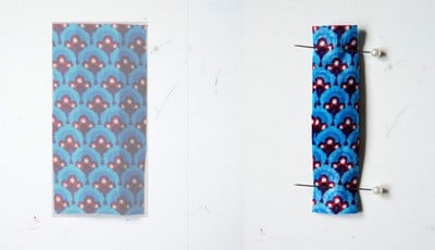 Stoffstück mit blauer, roter und weißer Musterung für eine Clutch, Nadel und Stecknadeln zum Zusammenstellen des Nähprojekts.