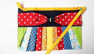 Bunte selbstgenähte Clutch mit buntem Stoffmuster, Reißverschluss und dekorativem Band, perfekt für den Sew Along Tag 4 - Clutch zusammenstellen.