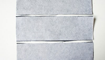 Drei Stoffstücke in verschiedenen Grautönen, vorbereitet für die Herstellung einer Clutch im Rahmen des Sew Along Tag 4.