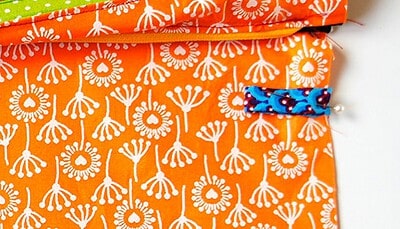 Bunte Clutch aus Stoff mit weißem Blumenmuster und blauer Schlaufe, ideal für DIY Nähprojekte, passend zum Sew Along Tag 4 - Clutch zusammenstellen.