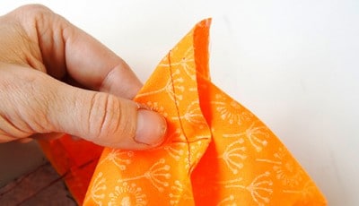 Detailaufnahme einer Hand, die eine orangefarbene Stofftasche mit weißen Mustern näht, im Rahmen eines Sew Along Projekts.