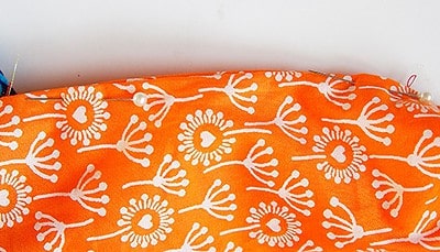Hochwertiger Stoff mit orangefarbenem Hintergrund und weißen floralen Mustern, ideal für die Herstellung einer Clutch im Sew Along Tag 4.