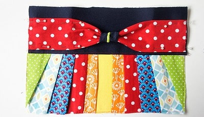Bunte Clutch aus Patchwork-Stoffen mit buntem Muster, Polka Dots, geometrischen Formen und einem schwarzen Band, perfekt für Handmade- und Nähprojekte.