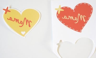 Herzförmige Anhänger mit handgeschriebenem 'Mama' in Rot und Gelb, ideal für Muttertagsgeschenke, handgemacht und liebevoll gestaltet.