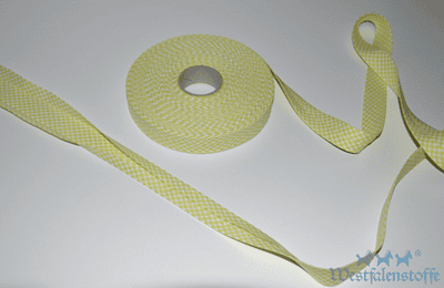 Gelbes Schrägband aus Stoff, zum Nähen und Verzieren von Textilien, mit einer Rolle und einem langen Bandabschnitt, ideal für kreative Handarbeiten.