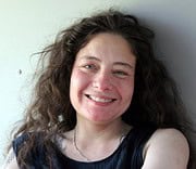 Lächelnde Frau mit lockigem Haar, die handgemachte Kunstwerke präsentiert, symbolisiert die kreative Atmosphäre von HANDMADE Kultur, Fokus auf Handarbeit und Kunsthandwerk.