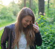Lächelnde junge Frau mit langen Haaren in einem schwarzen Lederjacke, umgeben von grünen Bäumen und Pflanzen im Wald, entspannt und glücklich in der Natur.