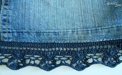 Detaillierte Nahaufnahme eines Jeansrocks mit handgefertigter Häkelspitze am Saum, zeigt die Textur des Denim und die filigrane Stickerei, perfekt für nachhaltige Mode.