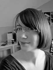 Porträt einer jungen Frau mit Brille, die kreative Handarbeit macht, im Hintergrund Werkzeuge und Materialien für handgemachte Kunstwerke sichtbar.