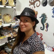 Frau mit schwarzem Hut in einem Laden voller bunter handgefertigter Kunstwerke und Dekorationen, darunter Seepferdchen und andere kreative Objekte.