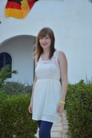 Frau in weißem Kleid steht neben grünen Pflanzen, mit einem deutschen Flaggenbanner im Hintergrund, bei Handmade Kultur Veranstaltung.