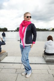 Modische Frau mit Sonnenbrille, pinkem Schal, Jeans und Blazer am Flussufer, entspannt und trendy, bei bewölktem Himmel, für Handmade Kultur SEO optimiert.