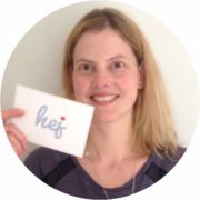 Frau mit blondem Haar hält eine Karte mit der Aufschrift 'hej' und lächelt freundlich, symbolisiert kreative Handwerkskunst und persönliche Begrüßung bei Handmade Kultur.