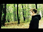 Frau in schwarzer Jacke steht im grünen Wald, umgeben von Bäumen, bei einem Spaziergang in der Natur, Fokus auf umweltfreundliche Kleidung und Naturverbundenheit.
