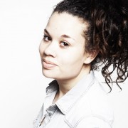 Frau mit lockigem, braunem Haar und natürlichem Make-up, trägt eine weiße Bluse, wirkt entspannt und freundlich, ideal für Handmade- und Kulturthemen.