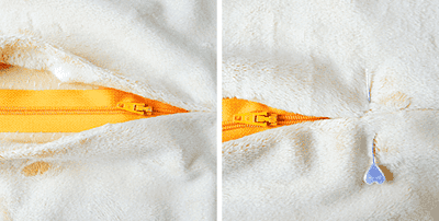 Nahaufnahme eines weißen Fleece-Pullovers mit orangefarbener Reißverschluss und Wasserfleck, Fokus auf die Textur und Details des Stoffes.