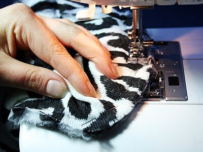 Hand beim Nähen eines Sattelbezugs aus Zebra-Print Stoff mit Nähmaschine, Fokus auf Stoff und Nähprozess.