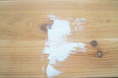 Holzoberfläche mit weißer Farbe, die ungleichmäßig aufgetragen wurde, zeigt natürliche Holzmaserung und Knoten.