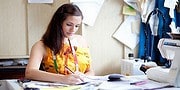 Junge Frau beim kreativen Arbeiten in einem Handwerksatelier, umgeben von Stoffen, Werkzeugen und Nähmaschinen, Fokus auf handgemachte Textilkunst und kreative Gestaltung.