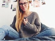 Junge Frau mit Brille in gemütlicher Kleidung sitzt entspannt und zeigt stolz ihre handgemachten Werke bei Handmade Kultur.