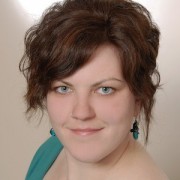 Porträt einer Frau mit kurzen, lockigen braunen Haaren und blauen Augen, trägt eine grüne Bluse, wirkt freundlich und selbstbewusst, ideal für handgemachte Kultur und kreative Themen.