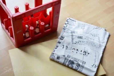 Getränkekiste als Sitzfläche für DIY Hocker, mit Stoff und Bastelmaterialien für nachhaltiges Möbelprojekt.