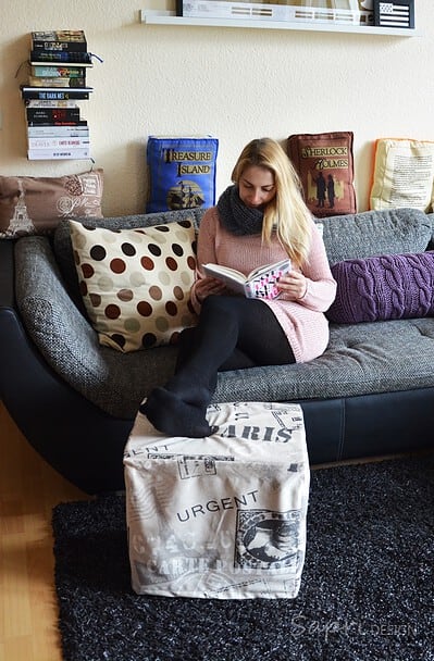 Frau liest auf einem selbstgemachten Upcycling-Hocker aus Getränkekisten in einer gemütlichen Wohnzimmer-Ecke mit Kissen und Büchern.