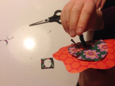 Hand beim Basteln von Papierblumen mit Schere, Kleber und buntem Papier, kreative Frühlingsdekoration aus Papier.