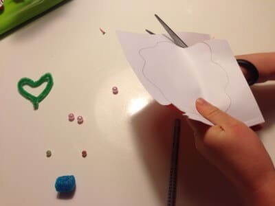 Hand beim Schneiden einer Papierblume mit Schere, bunte Perlen und Draht formen Frühlingsdekorationen aus Papier.