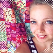 Junge Frau mit blauen Augen und gestreiftem Top vor buntem Quilt aus Patchwork-Stoffen bei Handmade Kultur.