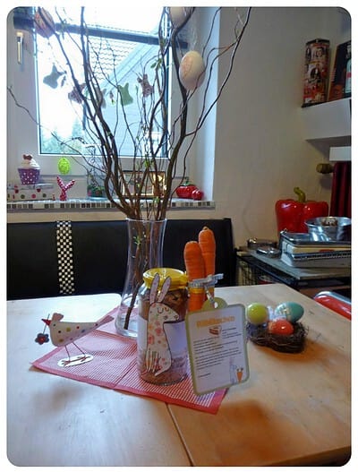Osterdekoration mit bunten Eiern, Zweigen und Hasenfigur auf einem Tisch, passend zur Frühlings- und Osterzeit, handgemacht und dekorativ.