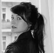 Schwarz-Weiß-Fotografie einer Frau mit dunklem Haar, die in die Kamera schaut, mit einem urbanen Hintergrund und einem Lederjacke, stilvoll und ausdrucksstark.