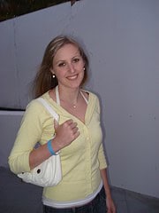 Junge Frau mit blondem Haar, gelbem Pullover und weißer Tasche, lächelnd bei Handmade Kultur Veranstaltung, zeigt Begeisterung für handgemachte Produkte.