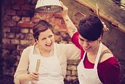 Zwei Frauen beim gemeinsamen Handarbeiten, lachen und Spaß haben, in einem kreativen Umfeld mit handgemachten Produkten, Fokus auf Handwerkskunst und Gemeinschaft.
