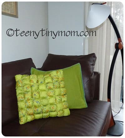 Zwei bunte Kissen, eines mit grüner Hülle und das andere mit gelber, auf brauner Couch im Wohnzimmer, mit Stehlampe im Hintergrund.