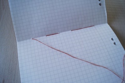 Bunte Fäden auf kariertem Notizbuch, kreative Bastelarbeit für handgemachte Kultur, DIY Projekt für bunte Notizbücher, Bastelideen für kreative Notizen.
